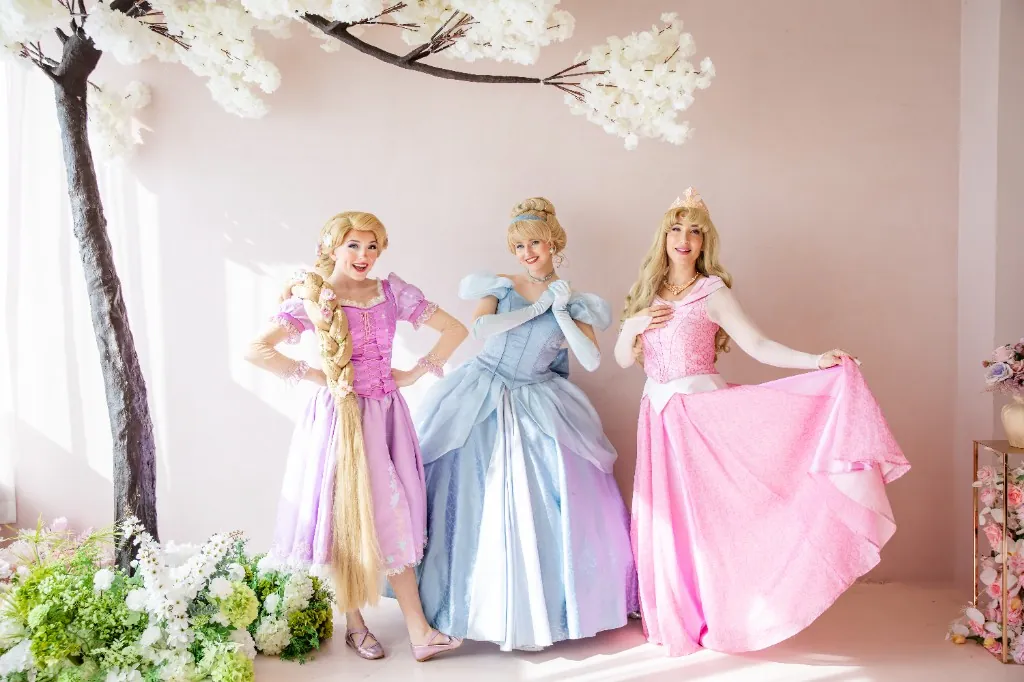 Three princess performers in pastel gowns beneath blossom branches